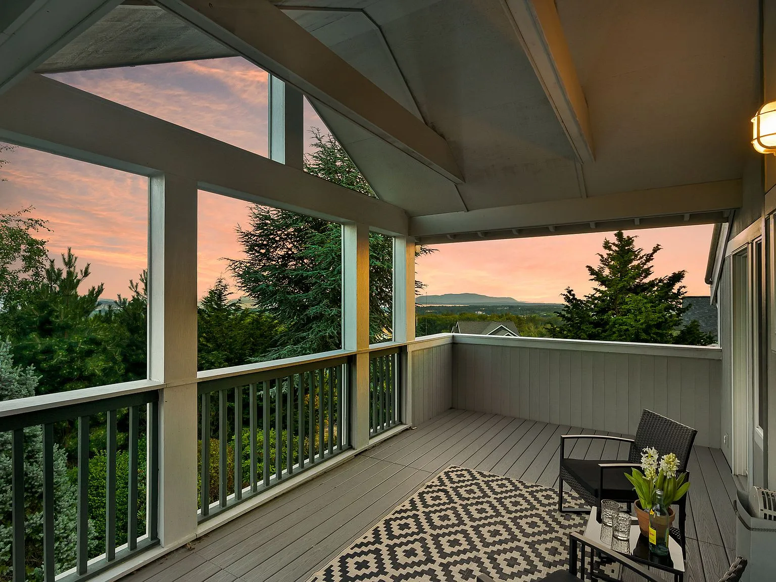 Covered upper deck at dusk with wicker seating, looking out over treetops toward distant mountains and the bay.