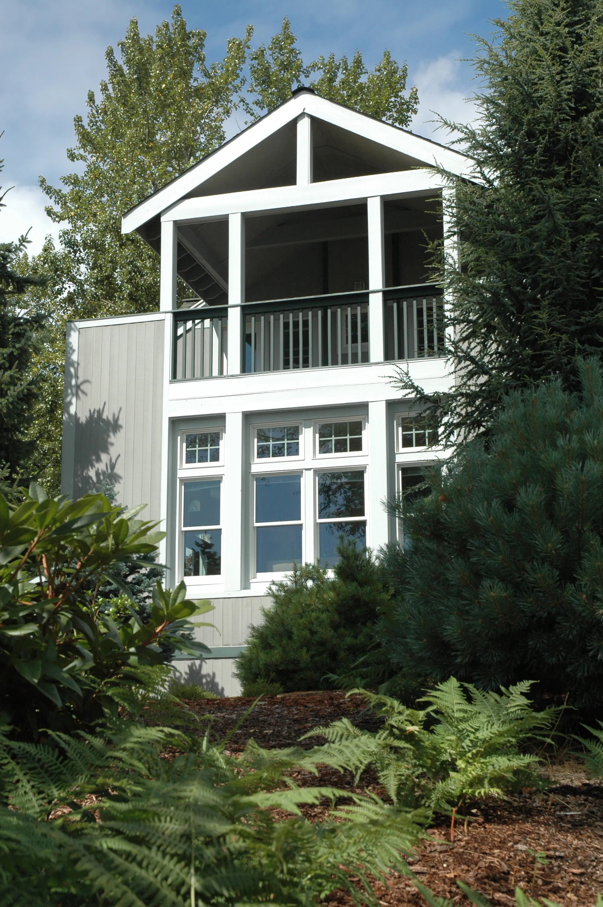 Close-up exterior view of the home's covered upper balcony framed by mature trees.