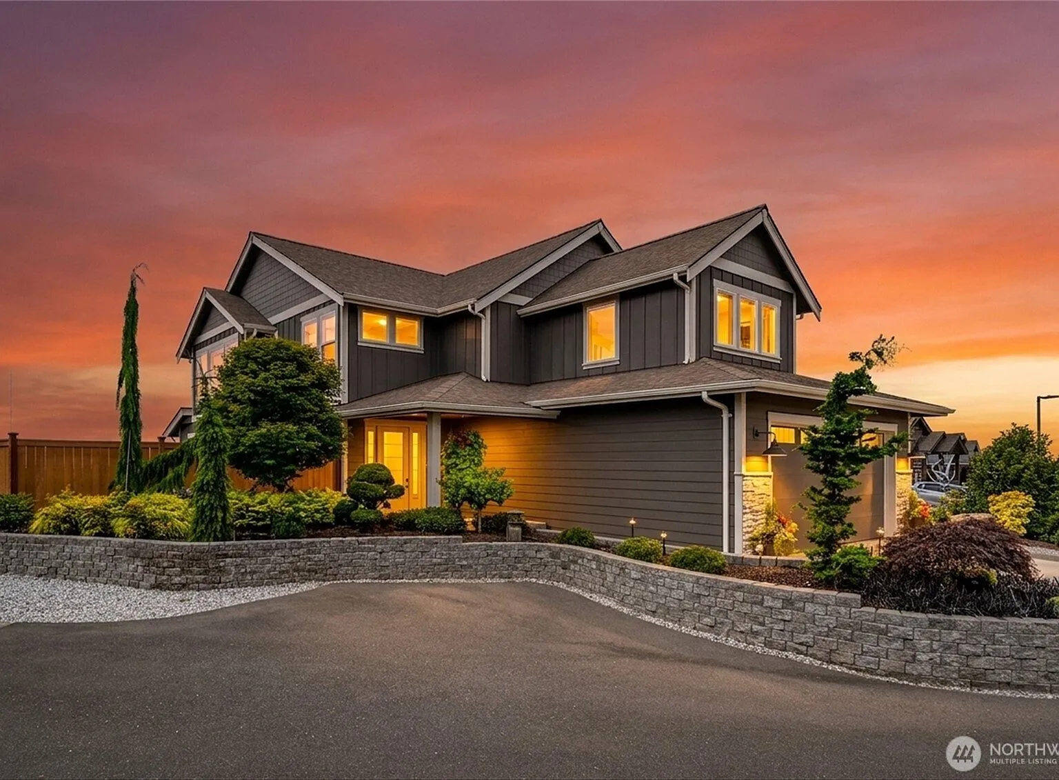 Rear patio at dusk with a fire pit and white Adirondack chairs, backed by tiered stone retaining walls and a lawn.