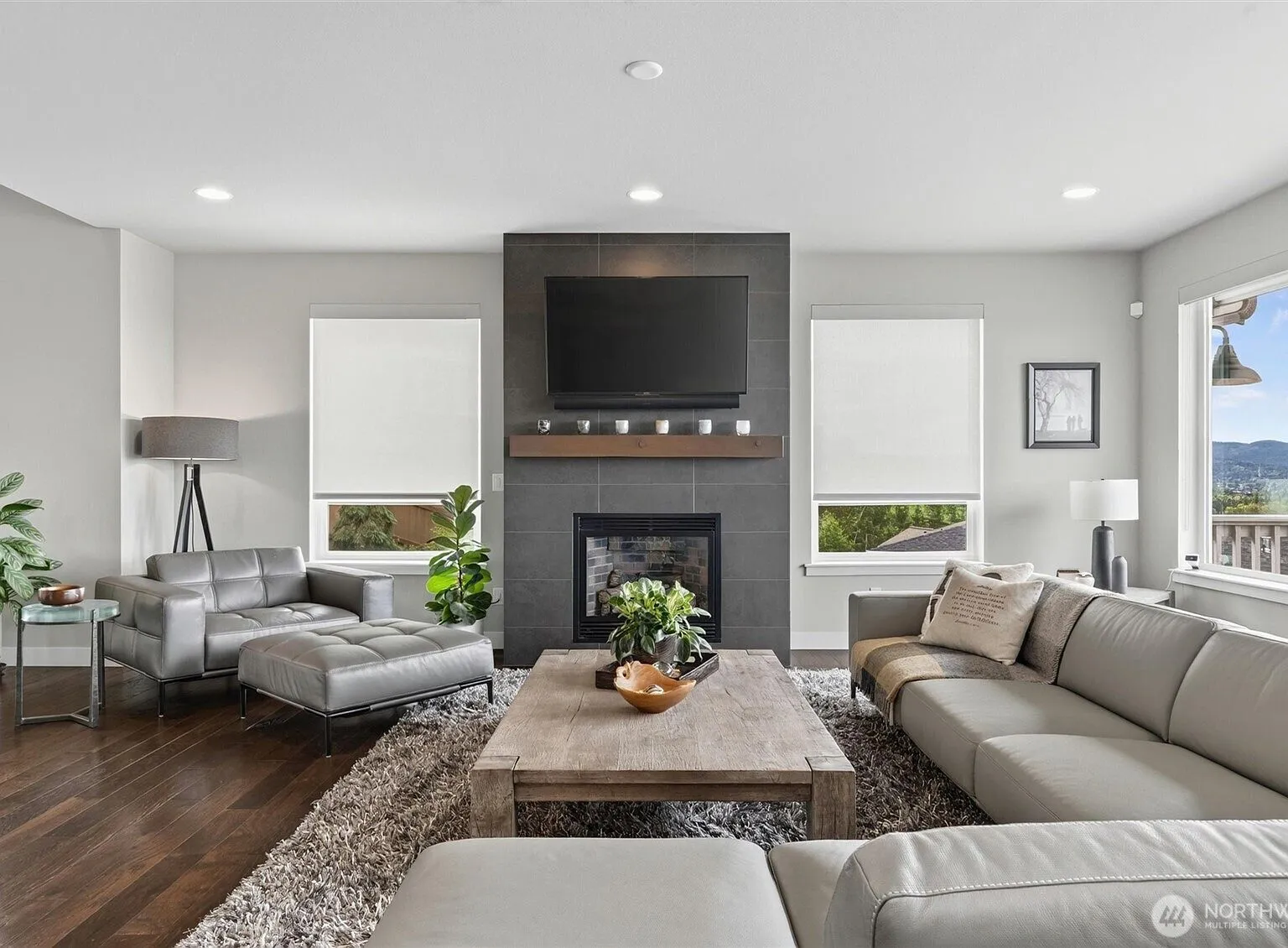 Living room with a tile-clad gas fireplace, wall-mounted television, and gray sectional sofa.