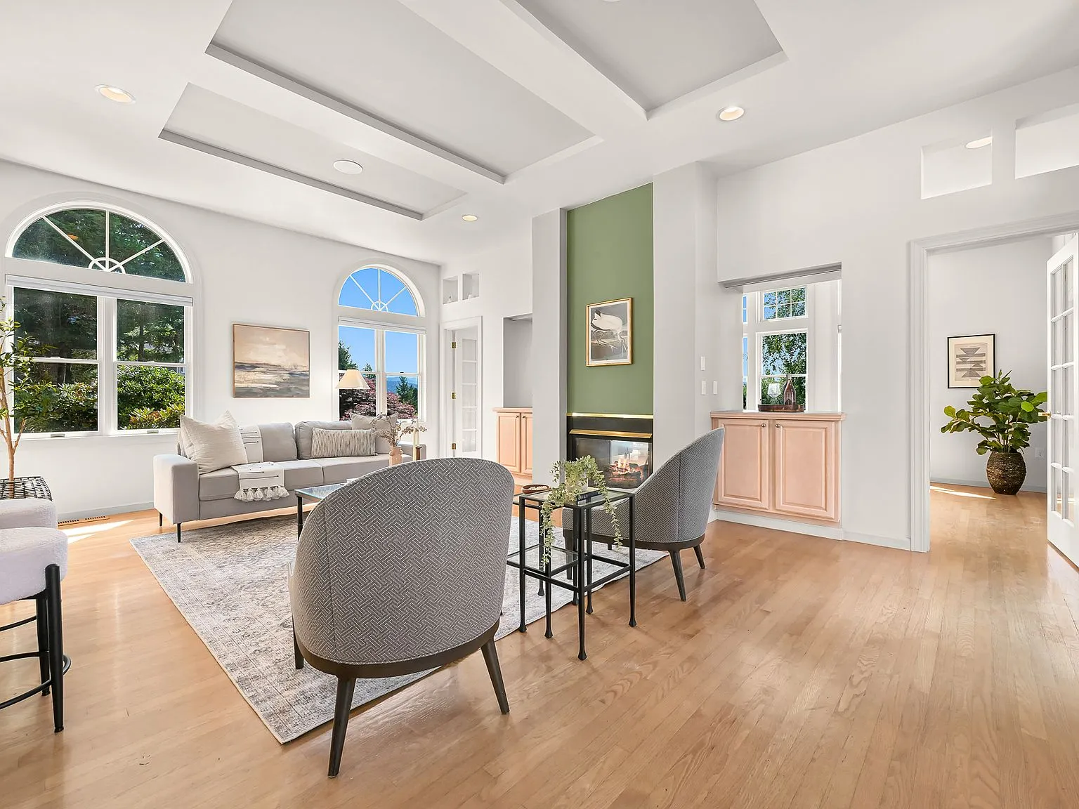 Living room with a sage-green gas fireplace surround, tray ceiling, and arched double-hung windows.
