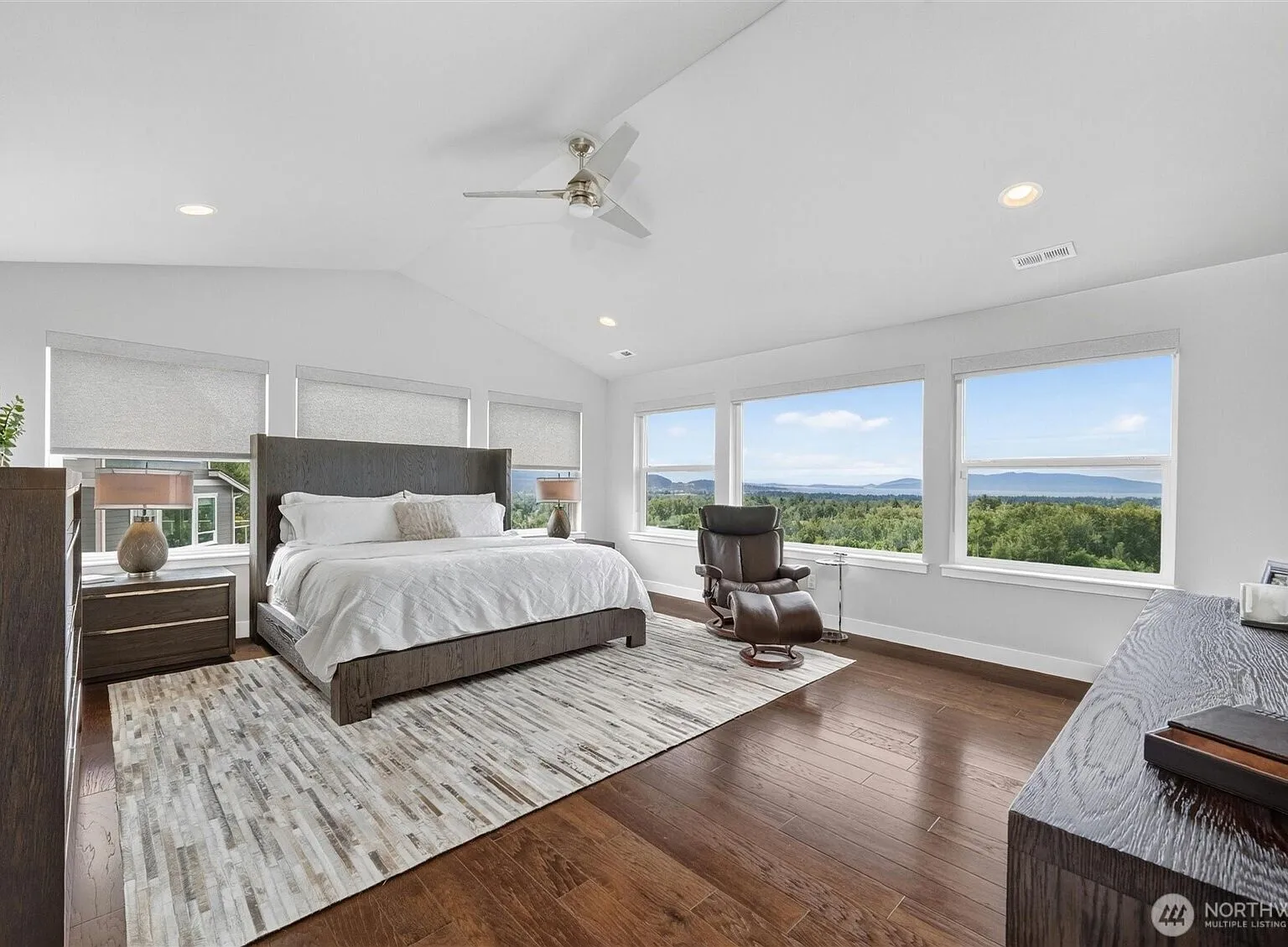 Vaulted primary bedroom with a wall of windows framing a panoramic view of the bay and mountains.
